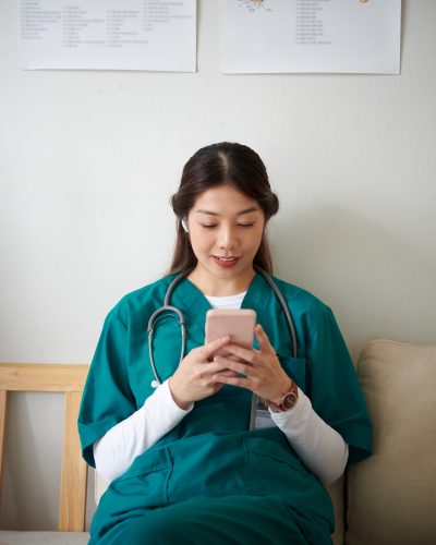 Young nurse sitting on couch in lounge area and texting friend or partner